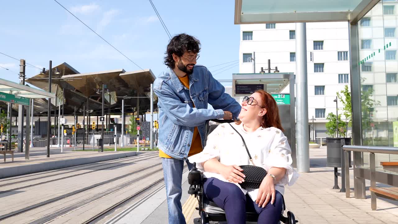Man assisting woman in wheelchair at tram station