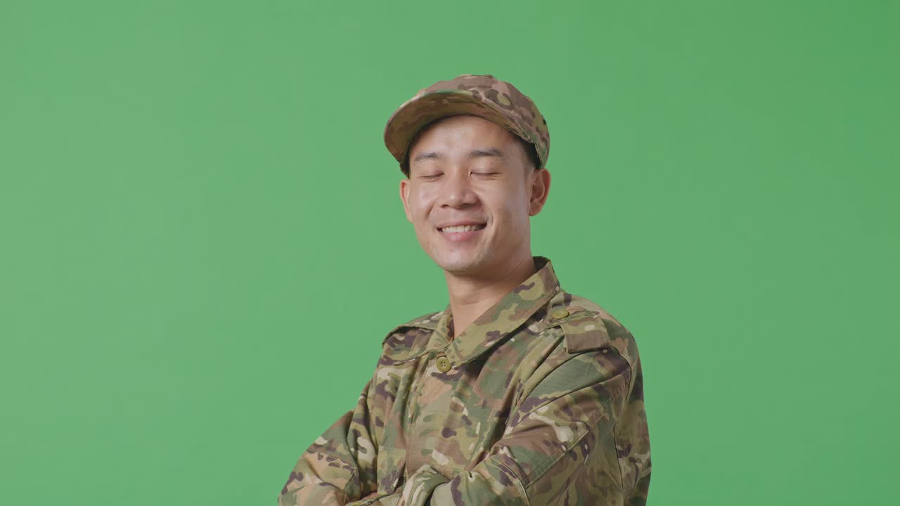 Close Up Of Side View Of Asian Man Soldier Smiling And Crossing His Arms While Standing In The Green Screen Background Studio
