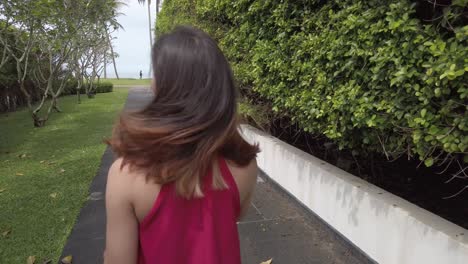 an asian young woman wear red dress carrying beach tote bag walking on pathwat to the beach paradise in summer vacation in slowmotion