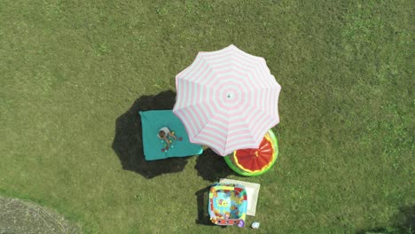 descending slowly above a small child playing in the shade of an umbrella on a hot sunny day, aerial