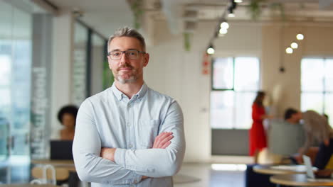 Portrait-Of-Serious-Mature-Businessman-Wearing-Glasses-Standing-In-Modern-Open-Plan-Office