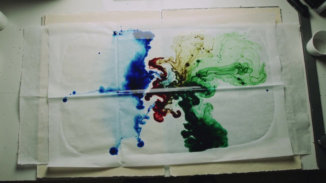 Tetesan mendarat memulai tinta biru, hijau, merah menyebar di lembaran yang direkatkan di meja, membentuk marbling