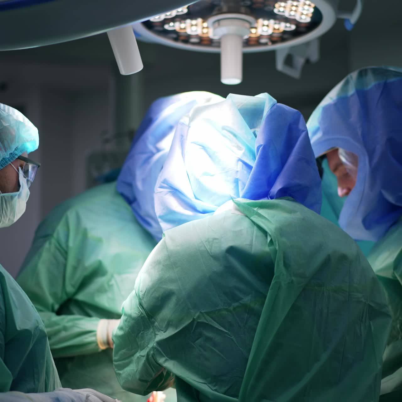 Three surgeons wear protective suits and helmets at operation. Assisting medic is wearing a mask, goggles and cap