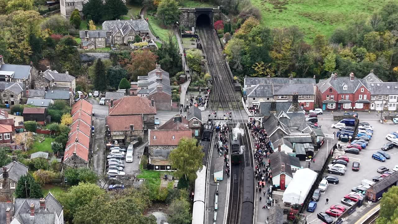 Aerial drone zoom in video of Pickering heritage railway station showing steam railway tracks, village buildings, trees, and autumn landscape in North Yorkshire England