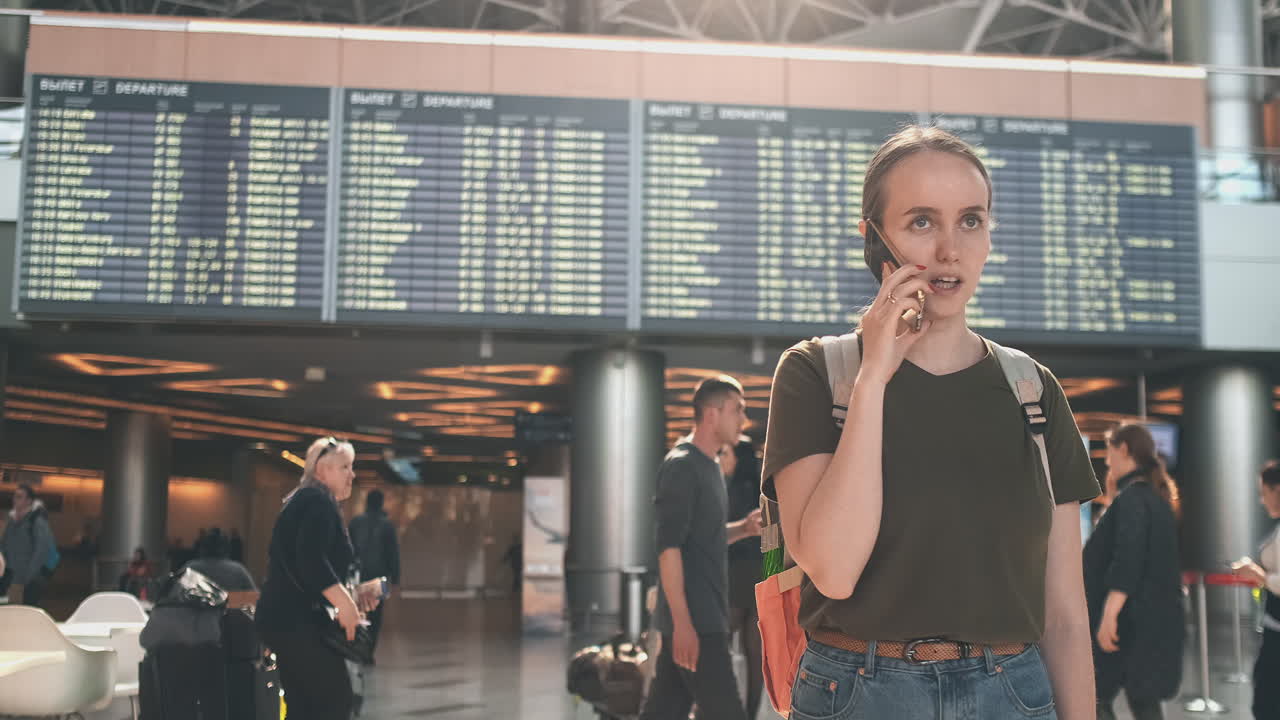 женщина-путешественник с рюкзаком в аэропорту обсуждает задержку своего рейса по телефону. трансфер и задержка отъезда из аэропорта
