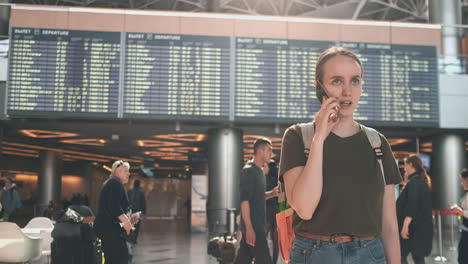 a woman traveler with a backpack at the airport discusses the delay of his flight on the phone. transfer and delay of departure from the airport