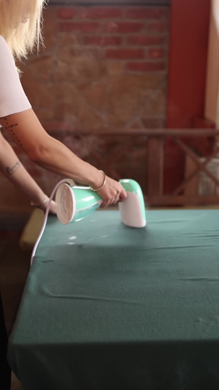 Woman Using Handheld Garment Steamer on Green Fabric