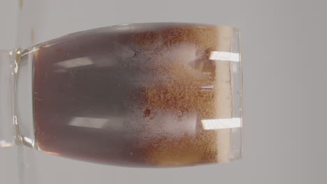 Ice-cubes-dropping-into-glass-of-cola-against-a-white-studio-background---vertical-video