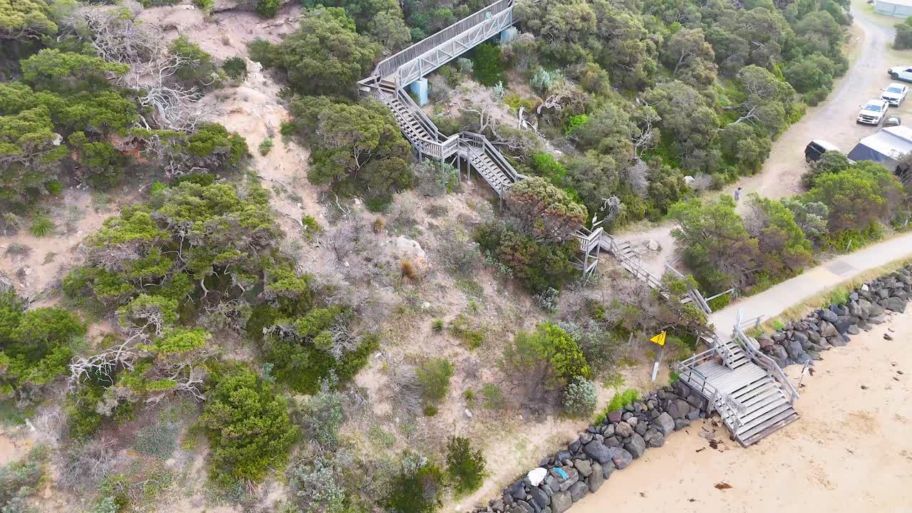 Drone footage captures a scenic coastal pathway with lush greenery and a sandy beach in Barwon Heads, Australia