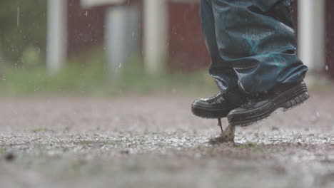 Zeitlupe---Ein-Kind-Mit-Regenschirm-Springt-Bei-Starkem-Regen-In-Die-Pfütze