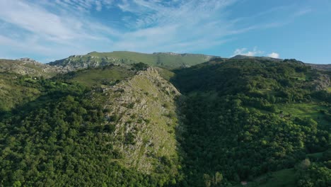 Vuelo-Lateral-Con-Dron-Sobre-Unas-Montañas-Haciendo-El-Efecto-Paralaje,-Desplazando-Algunas-Laderas-De-Piedra-Caliza-Con-Bosques-De-Robles-Y-Hayas-Con-Un-Cielo-Azul-Con-Nubes-En-Cantabria--españa