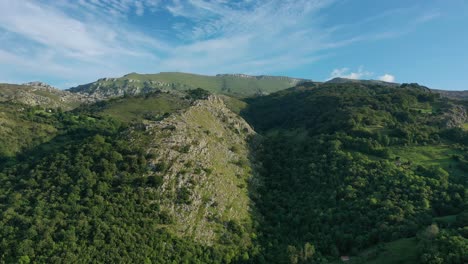 lateral flight with a drone over some mountains making the parallax effect, displacing some limestone slopes with oak and beech forests with a blue sky with clouds in cantabria -spain
