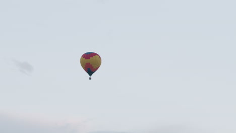 colorful hot air balloon carrying passengers floating peacefully in clear pastel sky at dusk, wicker basket hanging below vibrant yellow and red envelope panels drifting gently above distant horizon