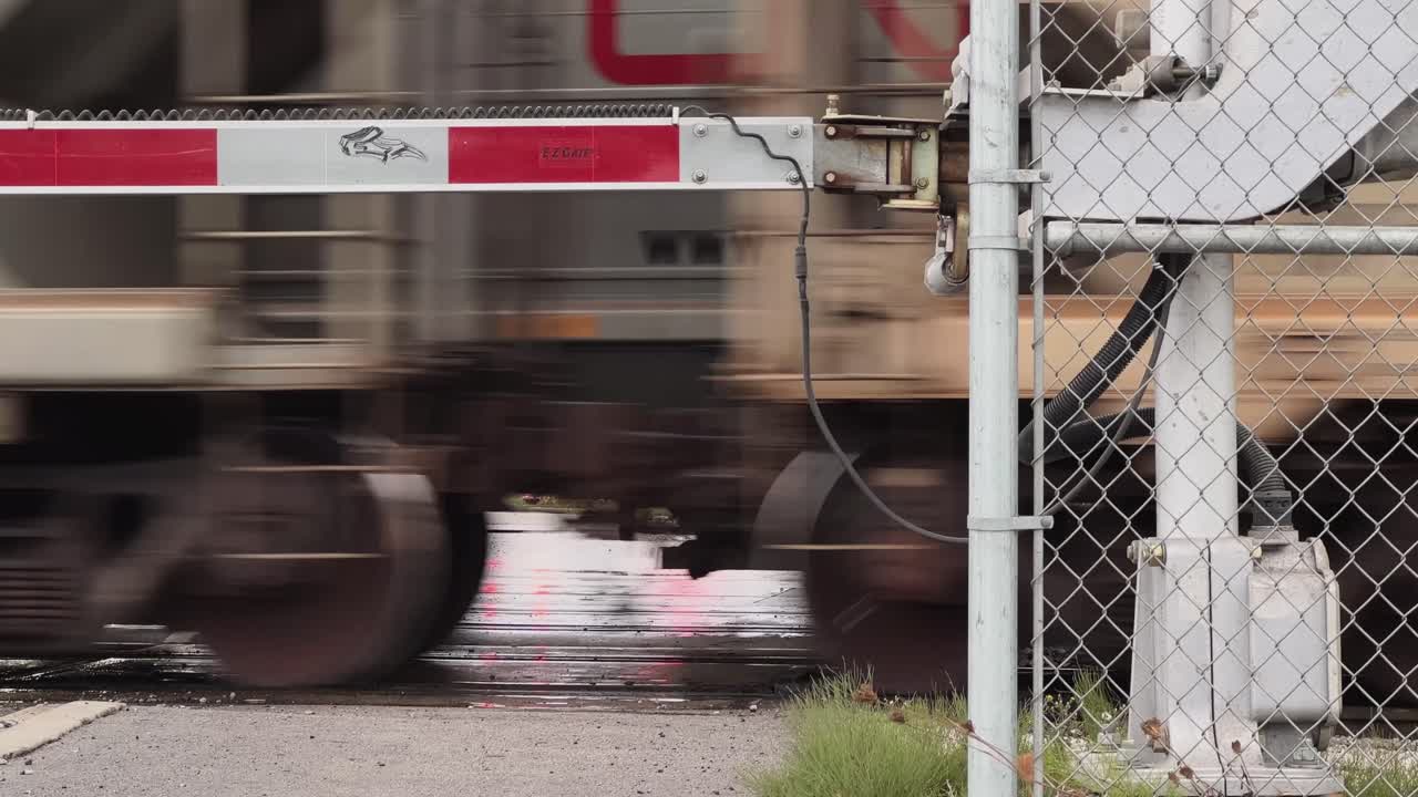 Two freight trains rush past in opposite directions behind the lowered crossing gate, wheels roaring as they blur together. A fast, layered moment of motion and metal