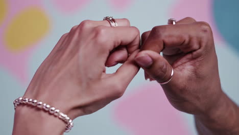 close-up of two diverse hands adorned with rings and a bracelet, interacting against a colorful, abstract background