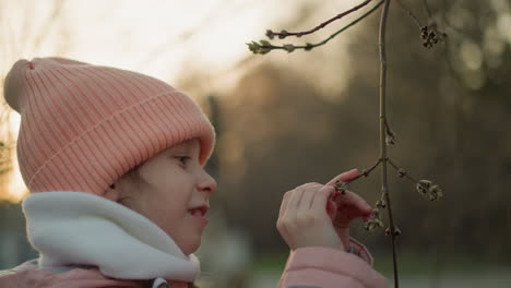 close-up of a little girl dressed in a pink jacket and beanie, intently playing with a dry tree branch. the image captures her curiosity and fascination with nature