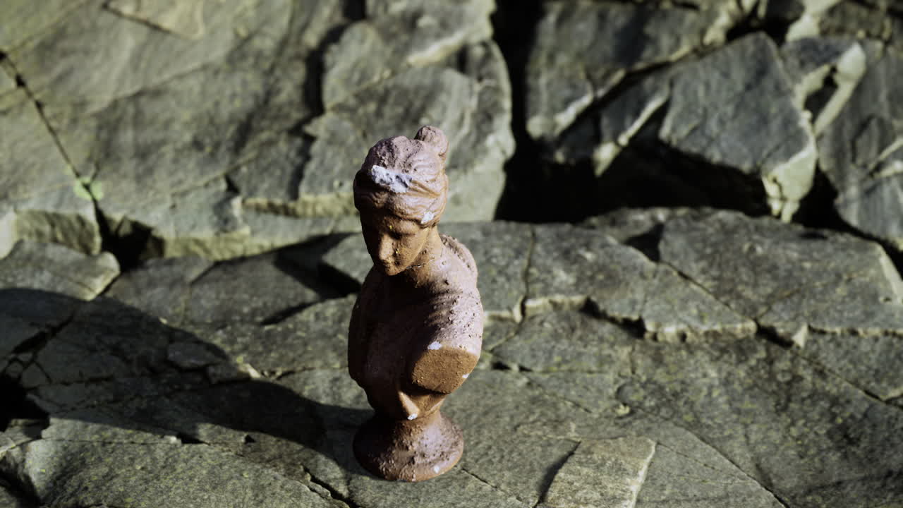 Small statue resting on rocky surface next to the sea