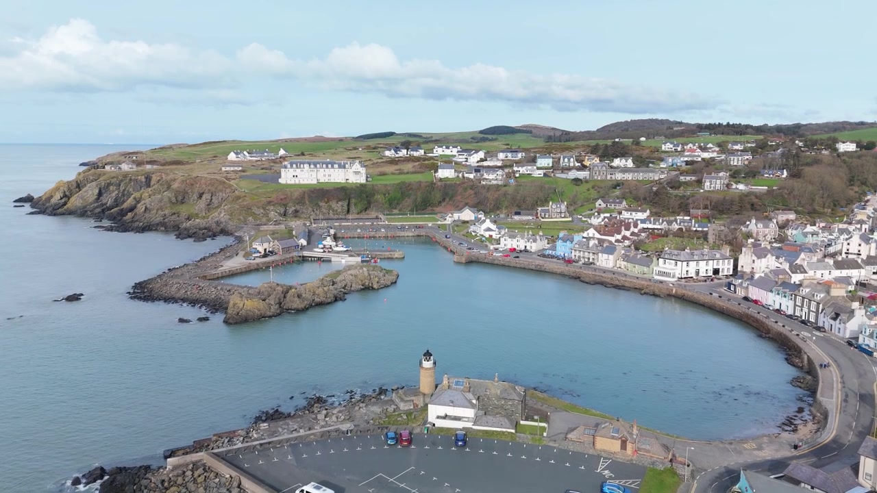 Movimento de dolly lento de drone desliza sobre o porto de Portpatrick, farol e cidade colorida.