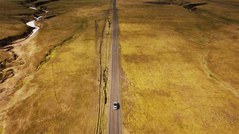 Drohne,-Die-Einem-Auto-Auf-Einer-Unbefestigten-Straße-Folgt,-Wobei-Die-Kamera-Langsam-Nach-Oben-Kippt-Und-Die-Landschaft-Von-Island-In-4k-Zeigt