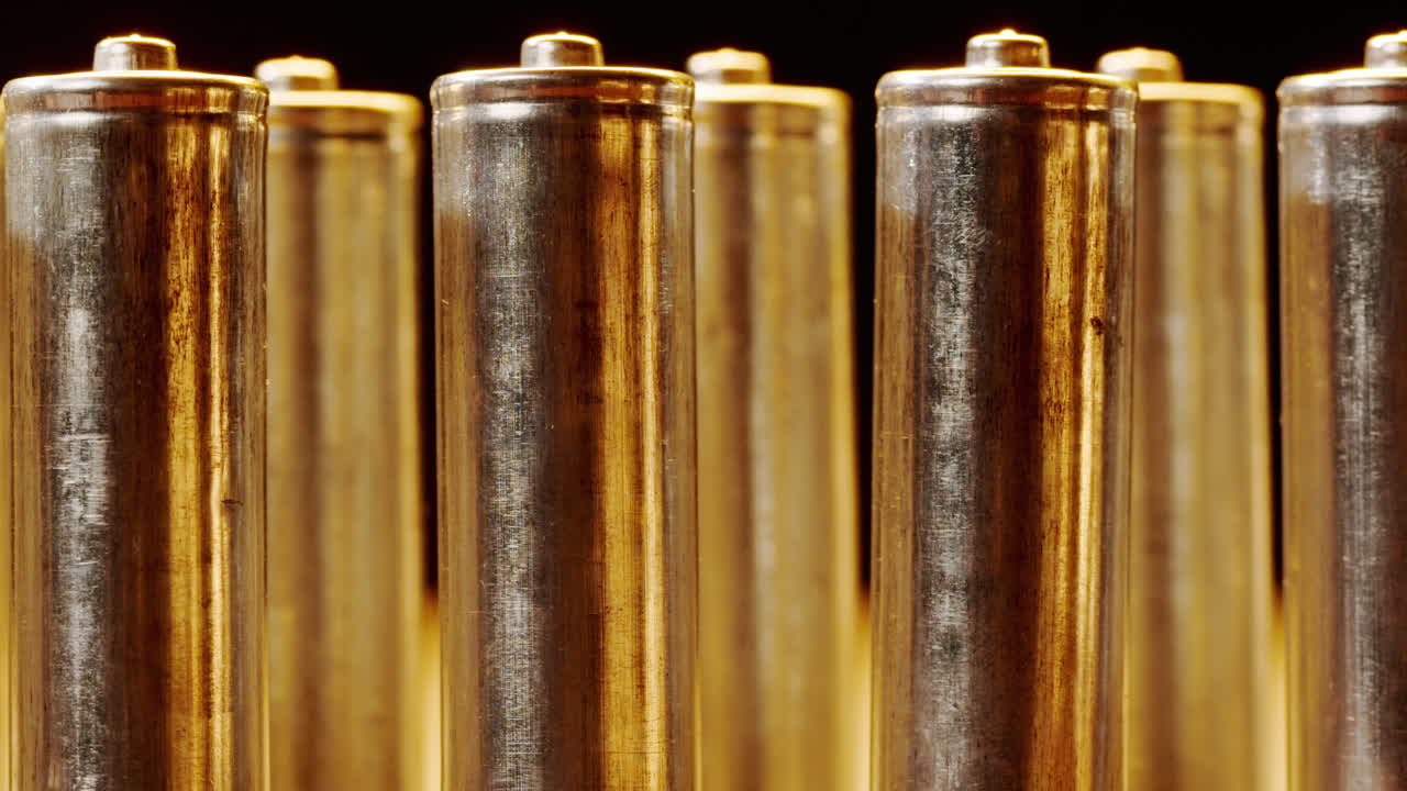 Silver batteries AA and AAA in neon light close-up. Double-A battery is a standard size single cell cylindrical dry battery. Batteries are common in portable electronic devices. An AA battery is composed of a single electrochemical cell that may be either a primary battery or a rechargeable battery.