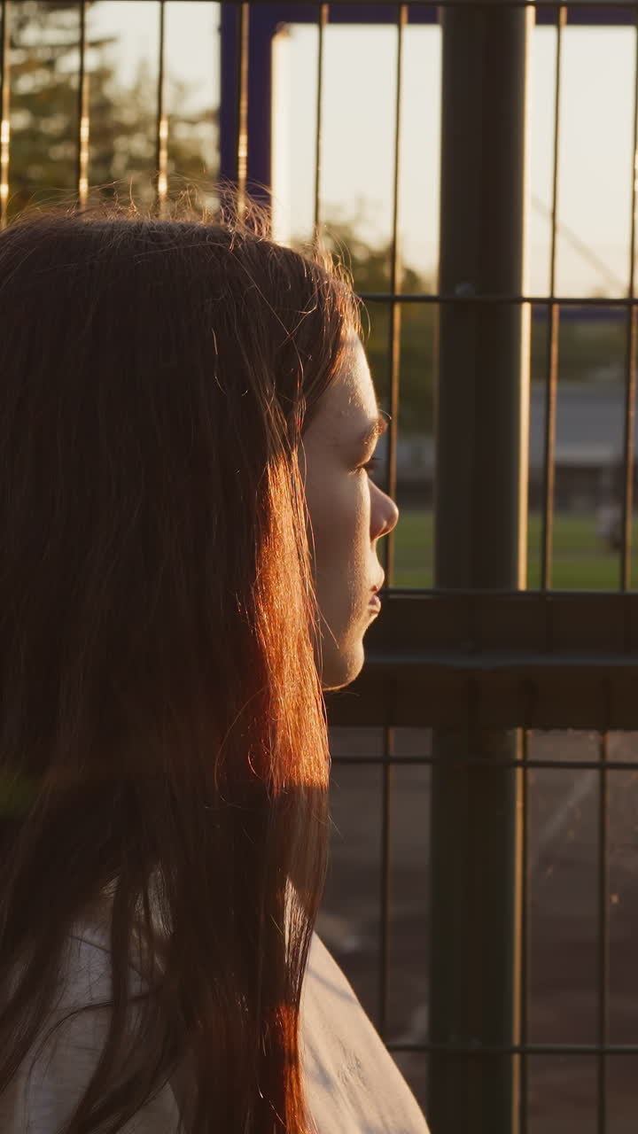 una mujer pasa por la valla mirando a los atletas. una joven infeliz ve a su ex novio caminando cerca del estadio después de hacer ejercicio al atardecer. se arrepiente de haberse separado.