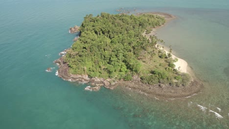 aerial ascending shot looking down on tropical island beach, jungle and rocky coastline