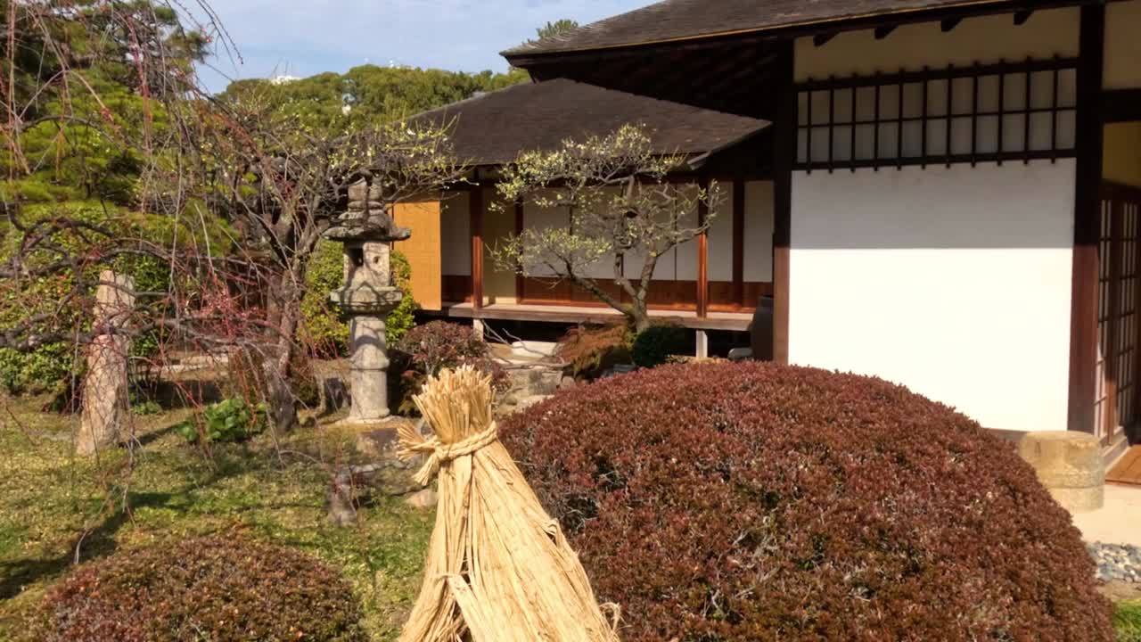 View of a traditional Japanese house facade featuring a stone lantern and manicured shrubs.