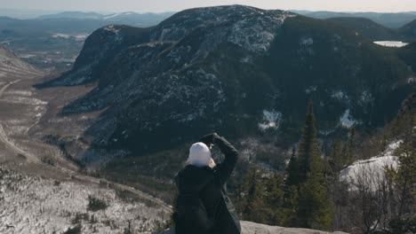 Girl-Sitting-On-Edge-Of-Mountain-Taking-Photos-At-Mount-of-the-Dome-In-Quebec,-Canada