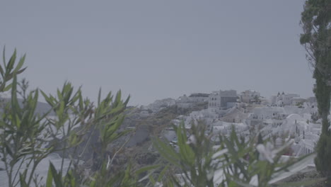 Überblick-über-Santorini,-Griechenland-An-Einem-Sonnigen-Tag,-Gesehen-Von-Einer-Terrasse-Mit-Pflanzen-Davor-In-Zeitlupe-Und-Dem-Meer-Im-Hintergrund,-Das-Den-Sonnenlogen-Reflektiert