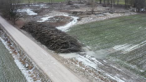 Aerial-approach-toward-pile-of-tree-branches-near-countryside-gravel-road