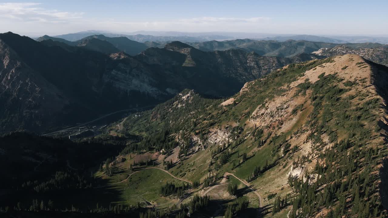 Vista aerea discendente che vola in una valle di montagna parzialmente ombreggiata nel mezzo di una grande catena montuosa nello Utah in una soleggiata giornata estiva