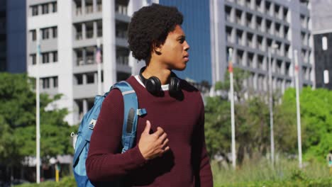 african american man in city checking smartwatch, wearing headphones and backpack waiting in street