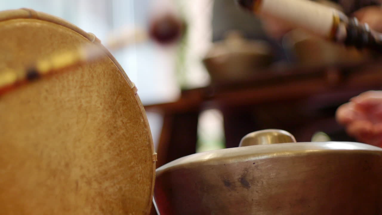Skinned drum and south east Asian bonang gamelan continuously struck by mallets during live performance, filmed as close up