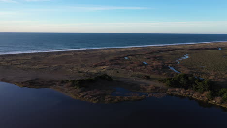 drone flying over the edge of floras lake, showing the pacific ocean divided by a strip of land, as well as the start of new river