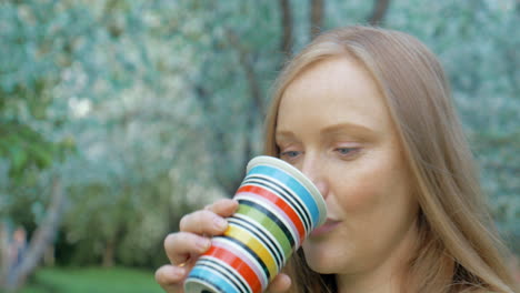 Mujer-Embarazada-Tomando-Una-Copa-En-El-Parque-Verde-Y-Florido