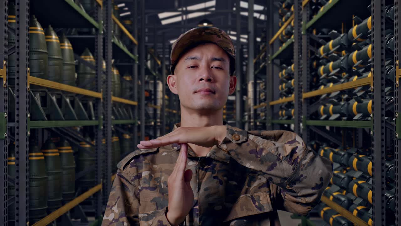 弾薬倉庫に立ち、タイムアウトのハンドジェスチャーを見せるアジア人男性兵士のクローズアップ.