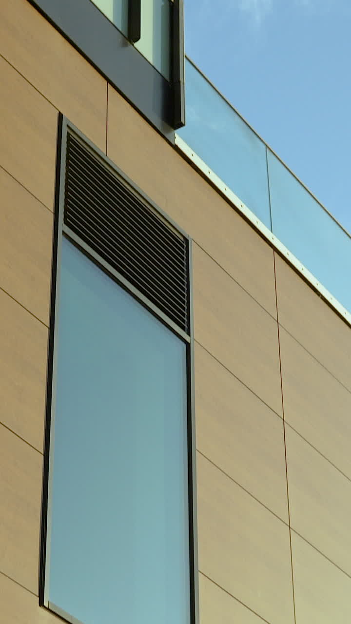 Un'inquadratura verticale inclinata di un edificio per uffici contemporaneo con pannelli di vetro e rivestimento color sabbia, contro un cielo azzurro limpido. Ideale per contenuti aziendali e immobiliari.
