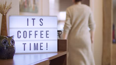 woman walks in and switches on decorative lightbox written its coffee time in comfy and cozy home