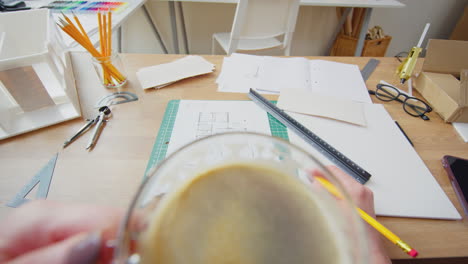 pov shot of female architect drinking cup of coffee working in office on plans for new building