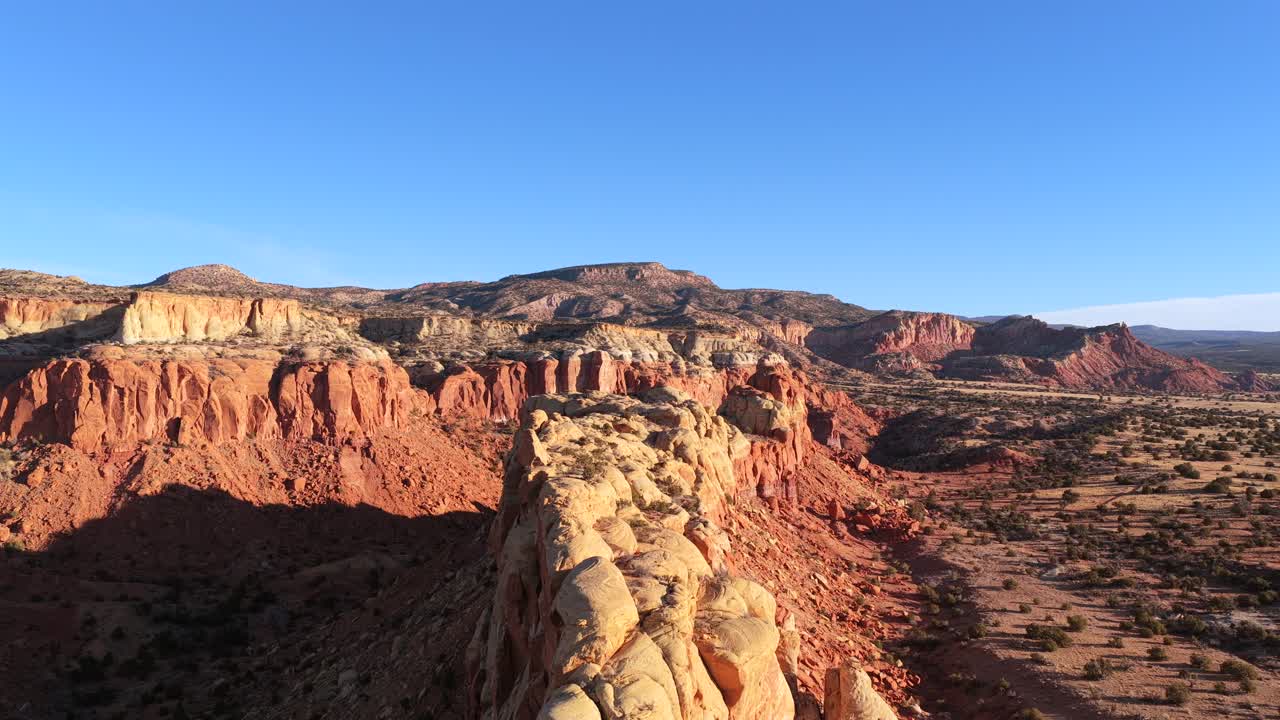 Una dinamica ripresa aerea segue la cresta di una affilata formazione rocciosa di arenaria nell'area di Abiquiu. Questa prospettiva unica cattura le aspre texture geologiche e la vasta natura selvaggia del deserto in straordinario 4K