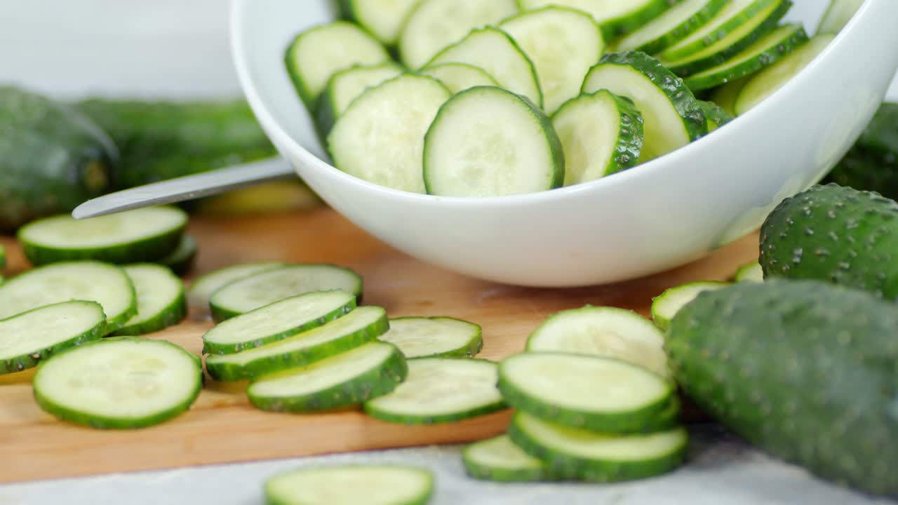 Sliced cucumbers on wooden cutting Board into the bowl.