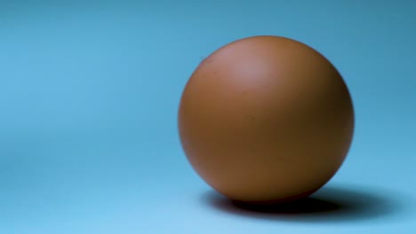 Close-up-shot-of-golden-chicken-egg-on-light-blue-background---can-be-used-as-a-loop