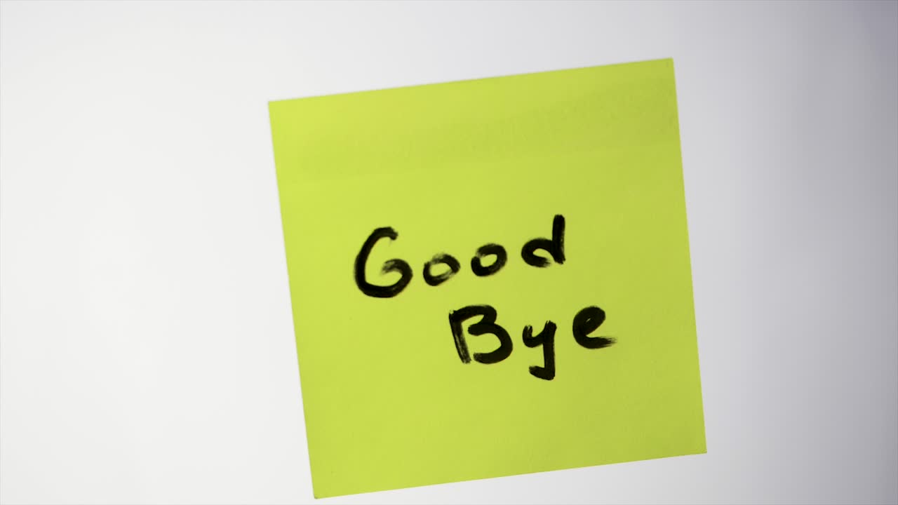 mano sosteniendo una nota adhesiva amarilla con las palabras "adiós" escritas en ella.