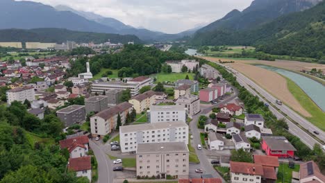 traffic on main street of swiss town with river and residential apartments. sunny day in summer. green idyllic village between alps in switzerland. aerial wide shot. rhine river