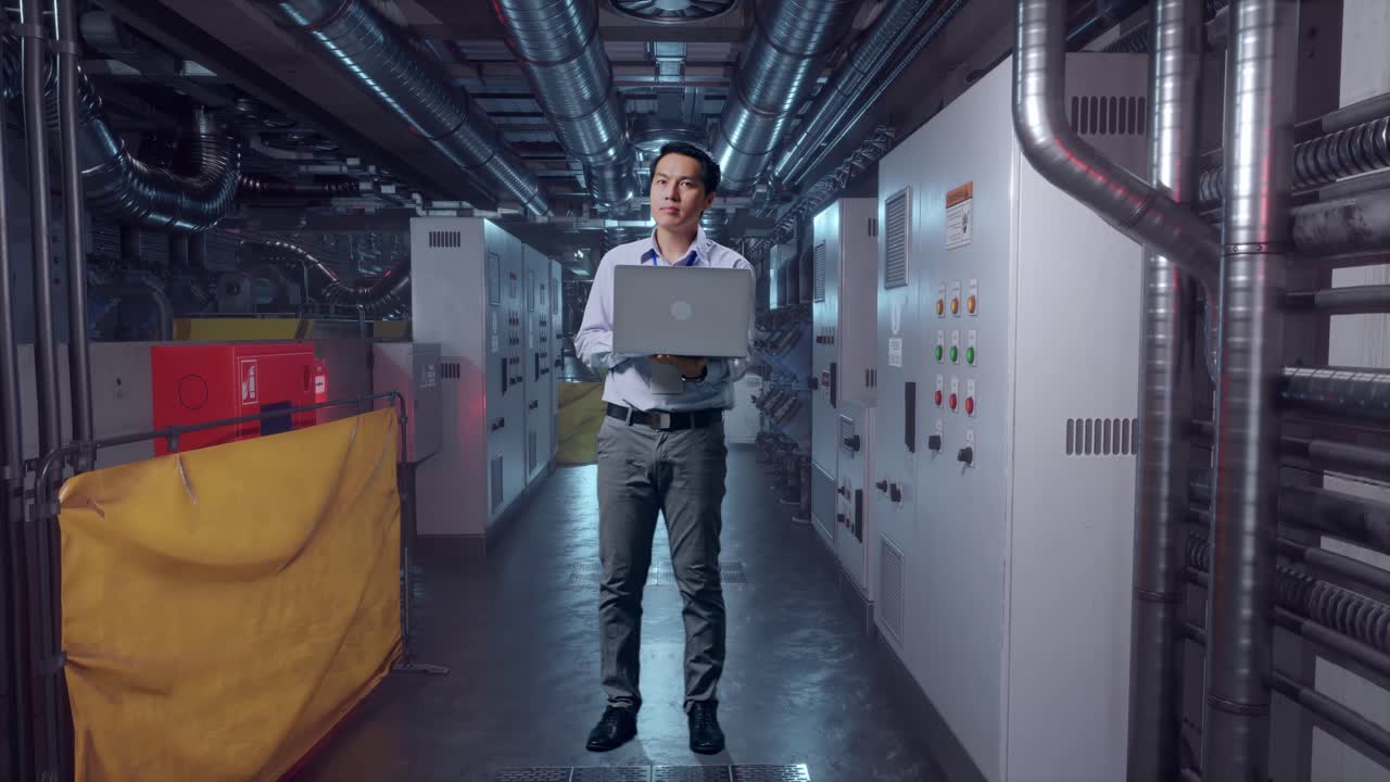 Full Body Of An Asian Male Professional Worker With His Laptop In Engine Control Room, He Observes By Looking Around Before He Come To Concentrating With His Laptop