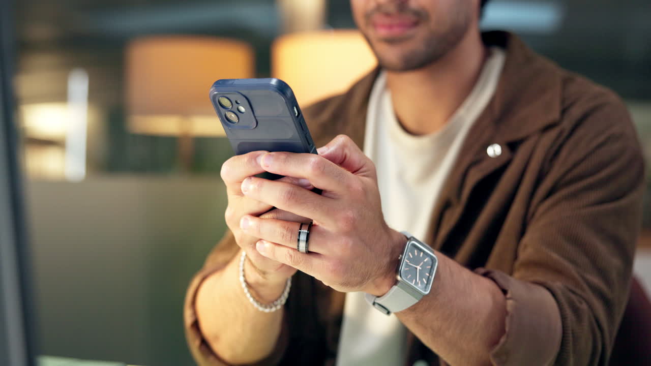 Uomo che usa lo smartphone e sorride al chiuso.