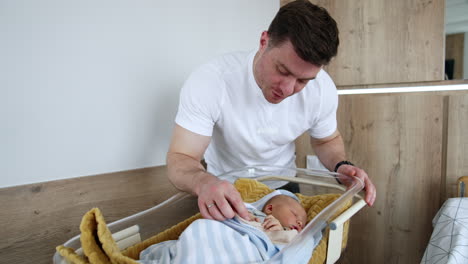dark-haired caucasian man stands over the baby crib in hospital ward. happy father taking care of his newborn son.