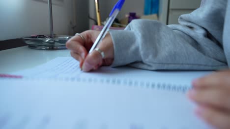 hand of female student writing notes on table, doing assignment at home