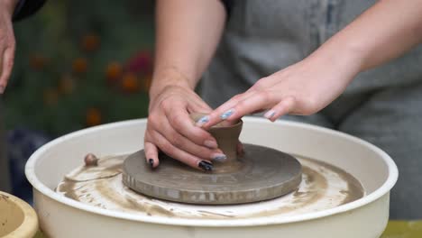 a young girl with a beautiful manicure is learning to make pottery on a potter's wheel. hands close-up.