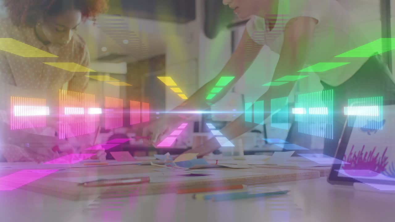 Mentor leaning over table arranging papers in design class, causing neon bars pulsing over tablet